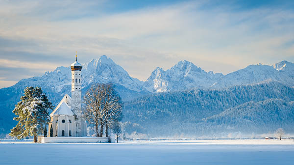 Winterpanorama der Kirche St. Coloman in Bayern, Deutschland mit schneebedeckten Alpen im Hintergrund von Michael Abid