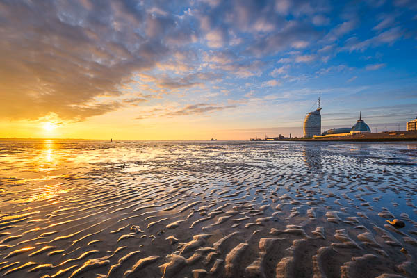 Weserufer bei Sonnenuntergang in Bremerhaven, Deutschland, mit dem Atlantic Hotel Sail City im Hintergrund, gespiegelt im Watt bei Ebbe von Michael Abid