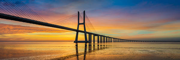 Panoramic view of the Vasco da Gama Bridge in Lisbon, Portugal during a beautiful sunrise, reflected in the Tagus river at low tide by Michael Abid