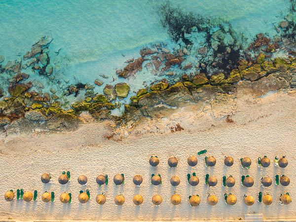 Aerial top-down view of Cala Millor beach in Mallorca, Balearic Islands, with sun loungers and parasols, a rocky shoreline and crystal-clear turquoise water, Spain by Michael Abid